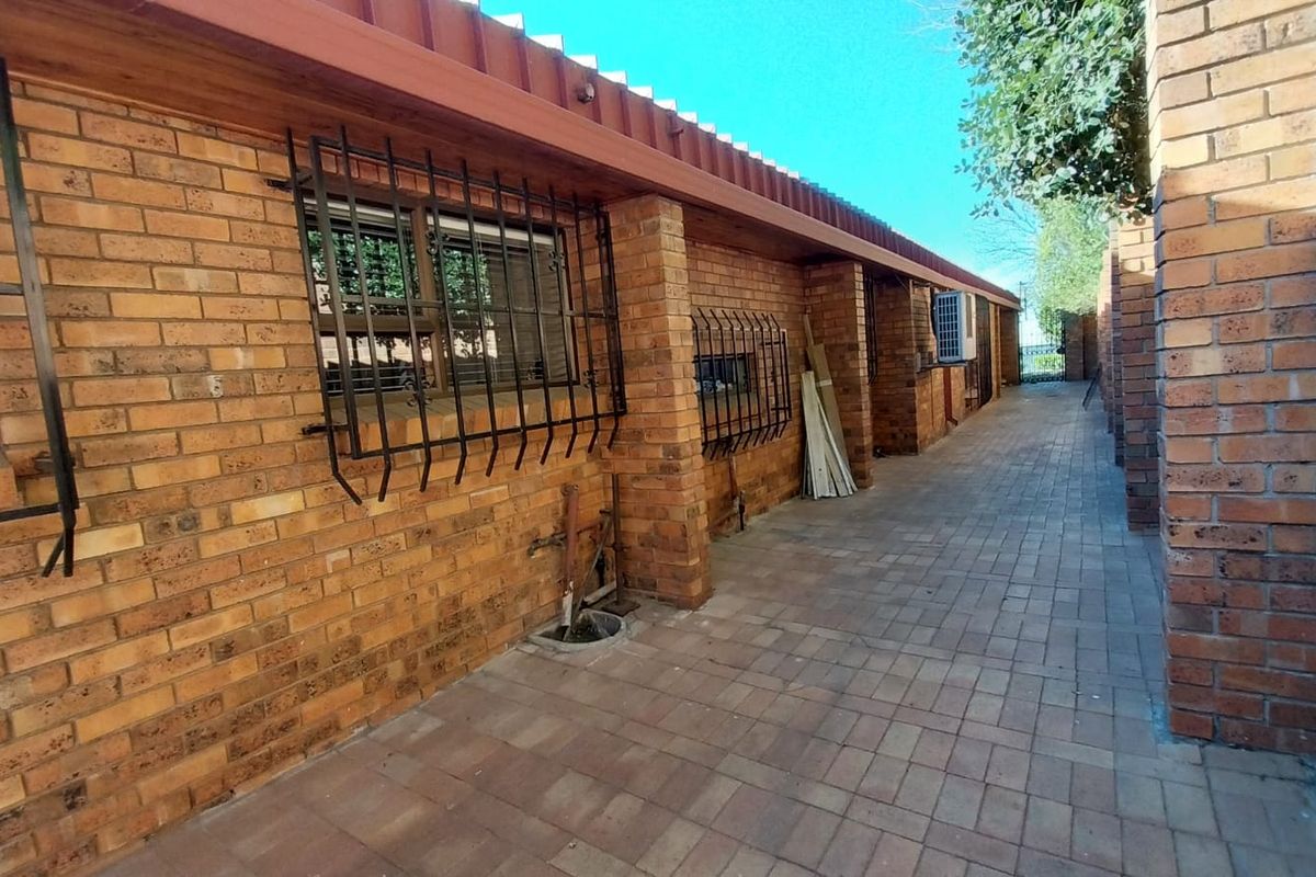 A side exterior view of the house featuring face-brick walls, security bars on windows, and paved walkway.