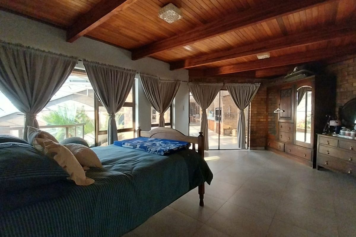 Spacious bedroom featuring exposed timber beam ceilings, tiled flooring, and large windows providing natural light and access to the outdoor area.