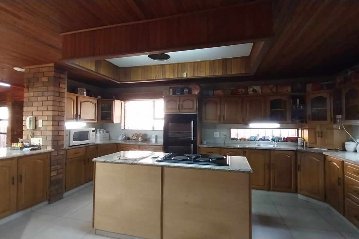 Spacious kitchen featuring extensive timber cabinetry, a central island with a built-in hob, and a distinctive timber-clad recessed ceiling.