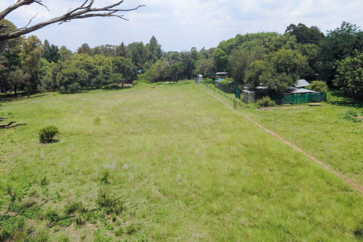 Aerial view of a large, open grassed small holding plot featuring established trees and perimeter electric fencing.