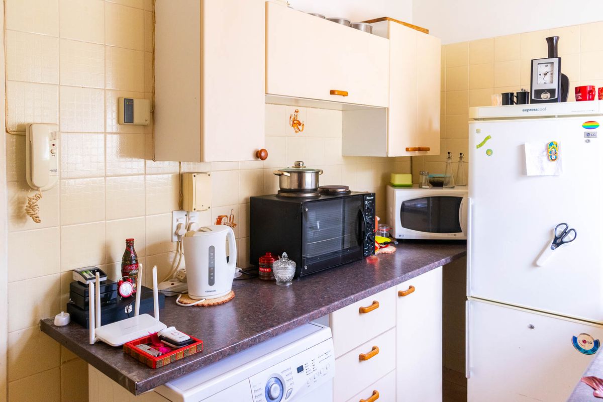 A compact kitchen area featuring dated cabinetry, tiled splashbacks, and laminate countertops, offering potential for a modern renovation.