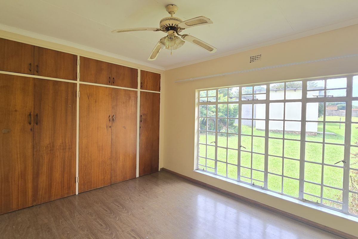 Spacious bedroom featuring extensive built-in wooden cupboards, a ceiling fan, and large windows overlooking the garden.