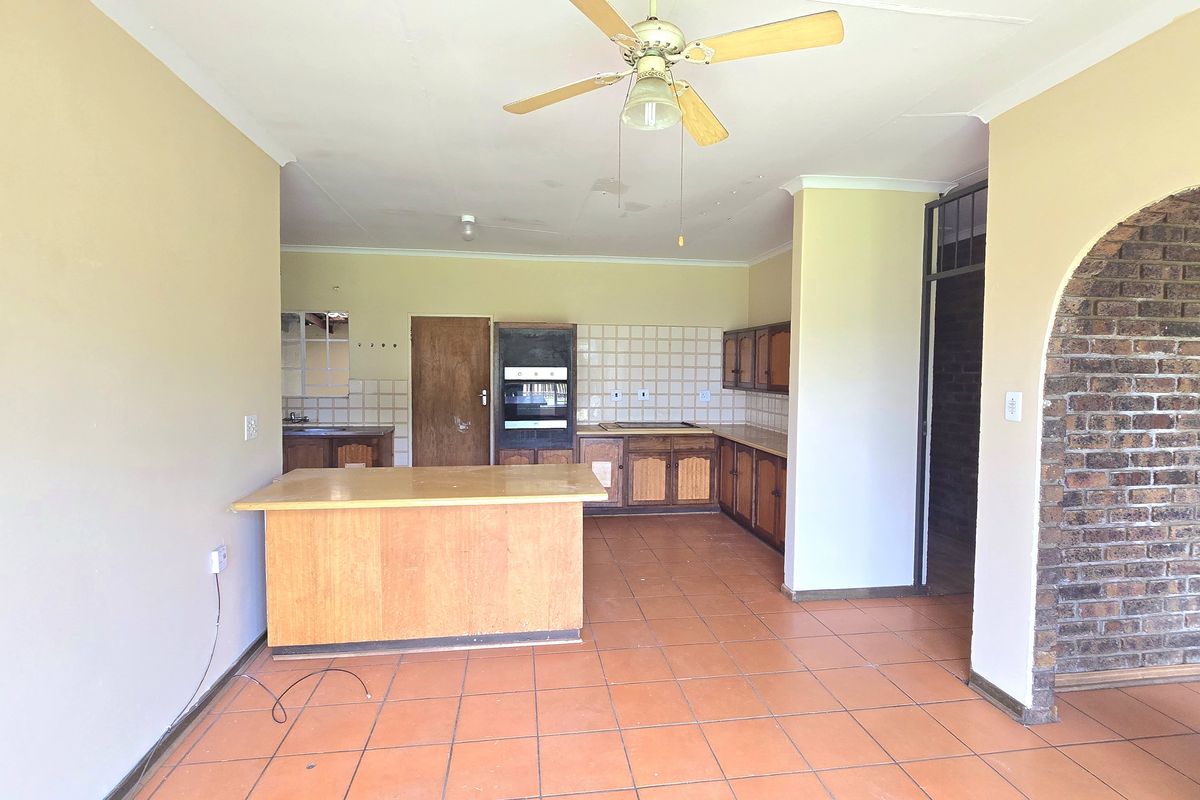 Spacious kitchen featuring wooden cabinetry, built-in oven, tiled flooring, and a distinctive brick archway, offering a functional layout ready for modern updates.