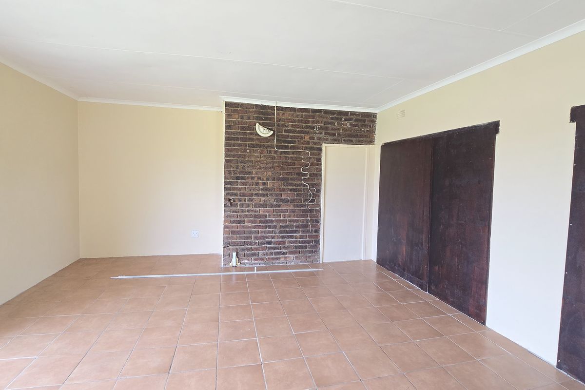 An empty living area featuring ceramic floor tiles, an exposed brick feature wall, and built-in sliding door storage.