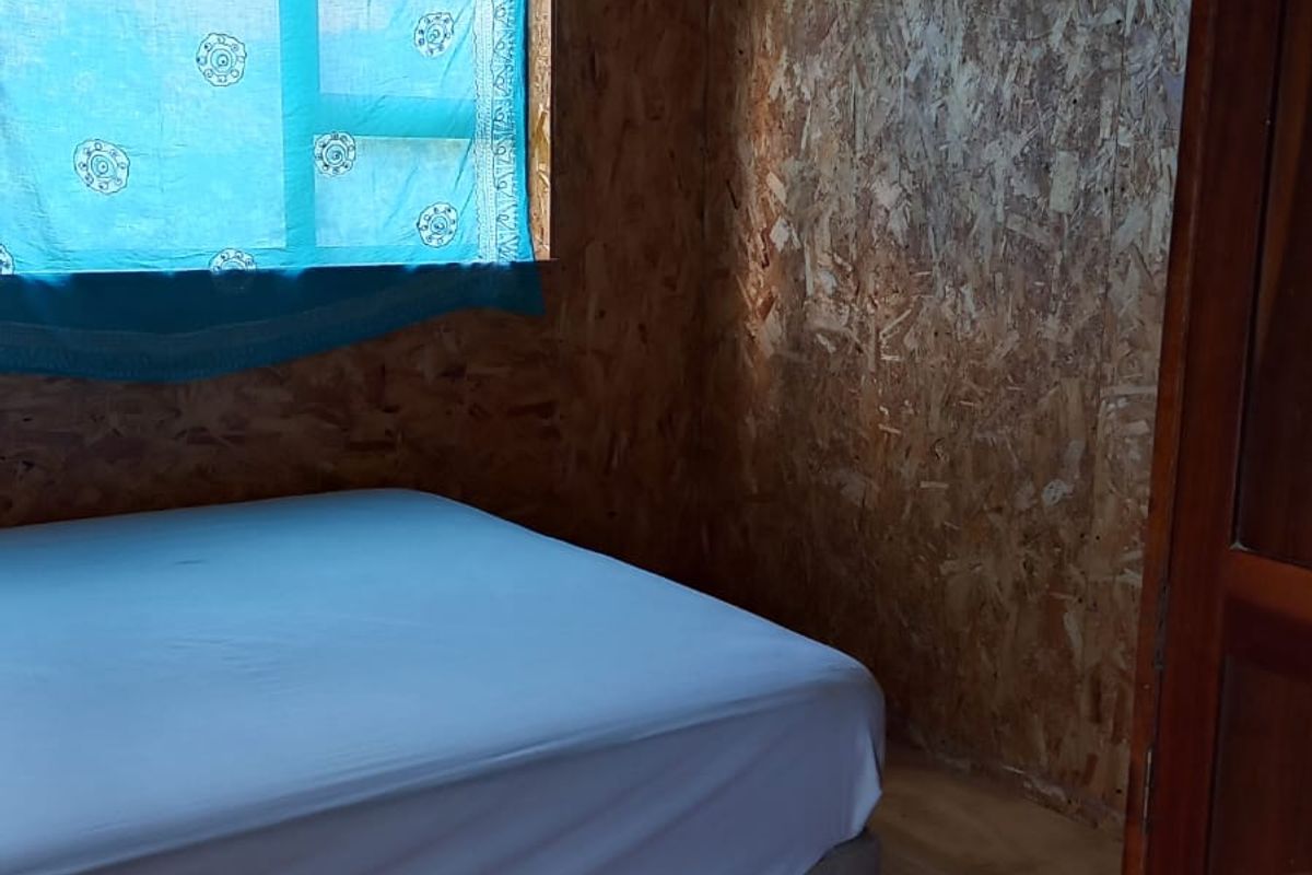 A bedroom featuring timber plank ceilings, oriented strand board wall paneling, and timber flooring, offering a rustic, unfinished aesthetic.