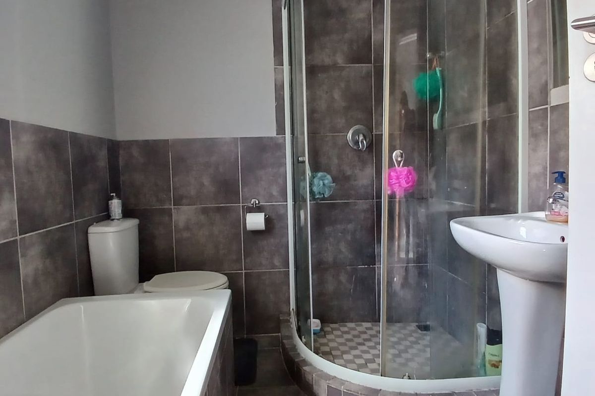 A functional bathroom featuring a pedestal basin, a curved glass shower enclosure, a built-in bathtub, and modern dark-toned wall and floor tiling.
