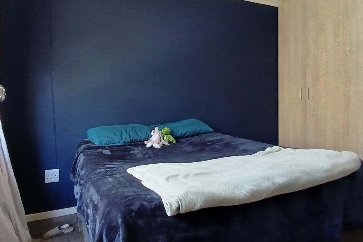 A bedroom featuring a dark blue accent wall and light-toned built-in cupboards, providing functional storage space.