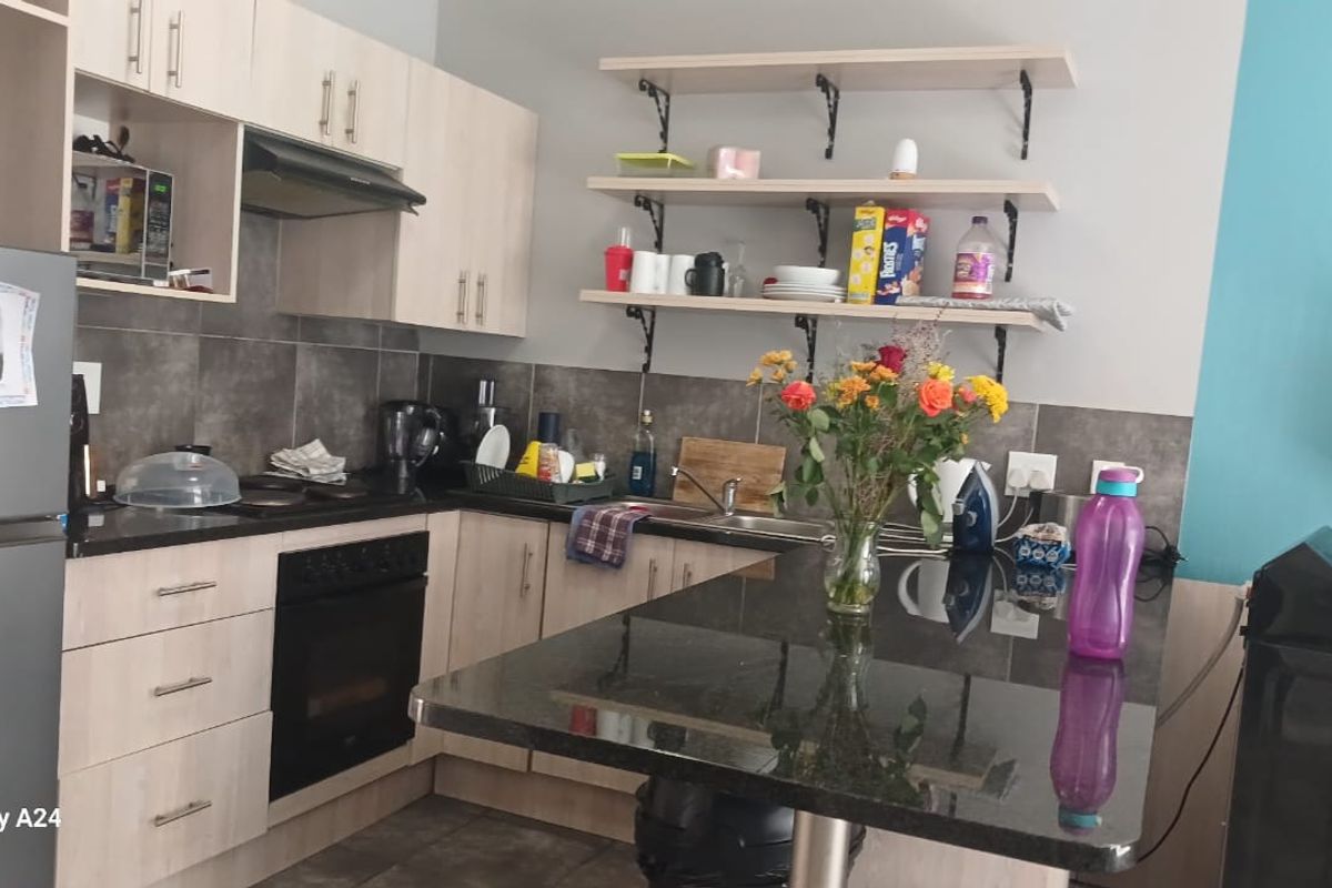 A functional kitchen featuring light wood cabinetry, dark granite countertops, a built-in oven, extractor fan, and open shelving with a tiled backsplash.