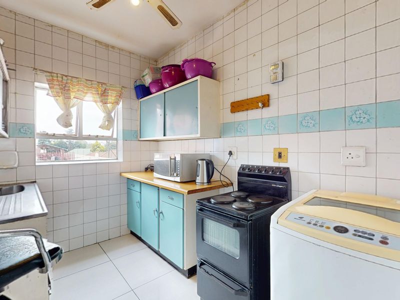 A functional kitchen featuring tiled walls, built-in cabinetry, a stainless steel sink, and an electric stove, offering potential for modernization and aesthetic updates.