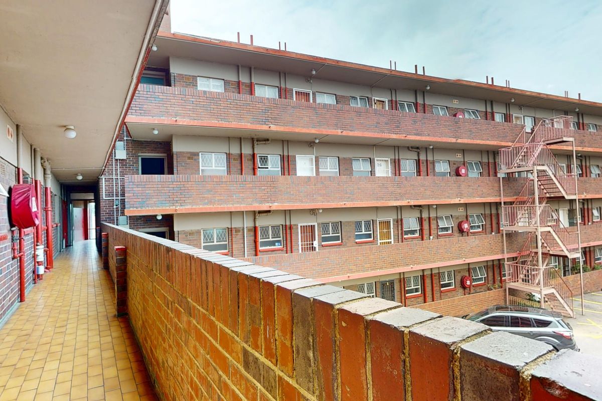 Exterior view of a multi-story apartment block featuring brick facade, external metal staircase, and tiled access walkways.