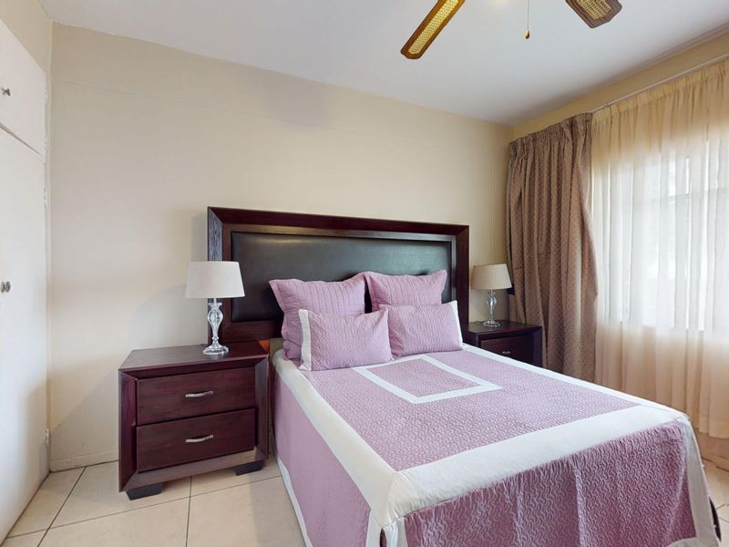 A bedroom featuring tiled flooring, built-in cupboards, and a ceiling fan, offering a functional and comfortable living space.