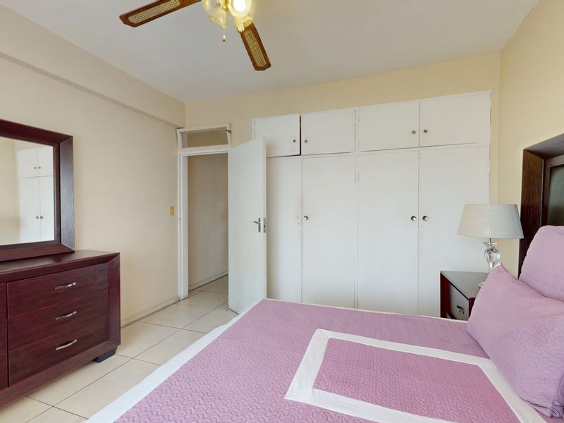 A bedroom featuring built-in cupboards, tiled flooring, and a ceiling fan, offering a functional and well-maintained living space.