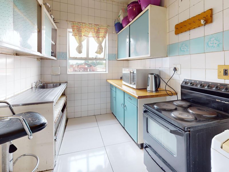 A dated kitchen featuring tiled walls and floors, built-in cabinetry, and a freestanding electric stove, offering significant potential for modernization and renovation.