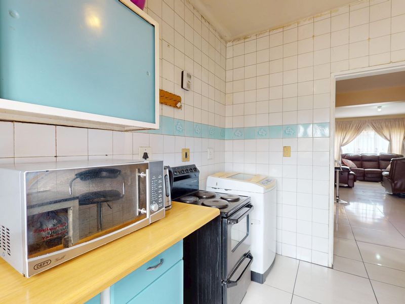 A dated kitchen featuring tiled walls, laminate countertops, and built-in cabinetry, with an adjacent view into the living area.