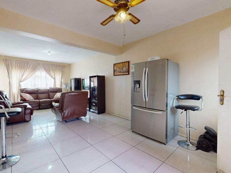 An open-plan living area featuring tiled flooring and a ceiling fan, providing a functional space that connects the kitchen and lounge areas.