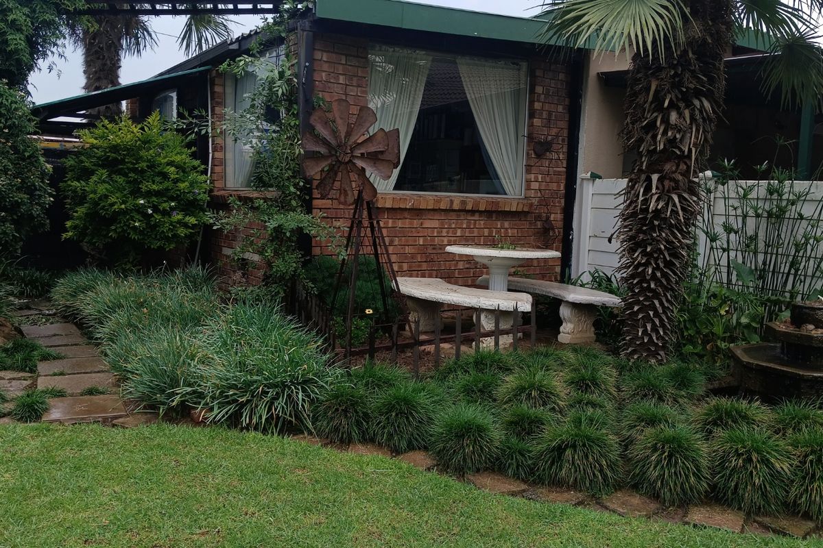 A view of the rear garden featuring a brick facade, established landscaping, a small water feature, and a paved outdoor seating area.