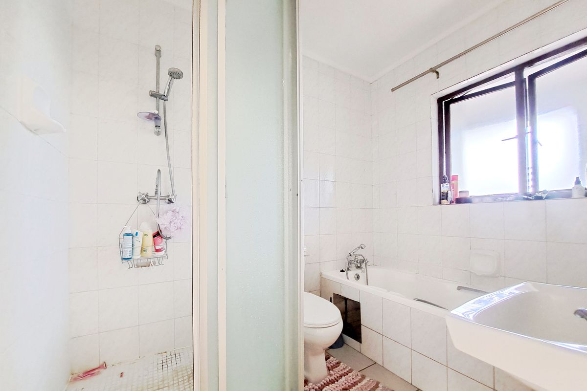A functional bathroom featuring a separate shower enclosure, bathtub, toilet, and tiled finishes throughout, offering a practical layout for daily use.
