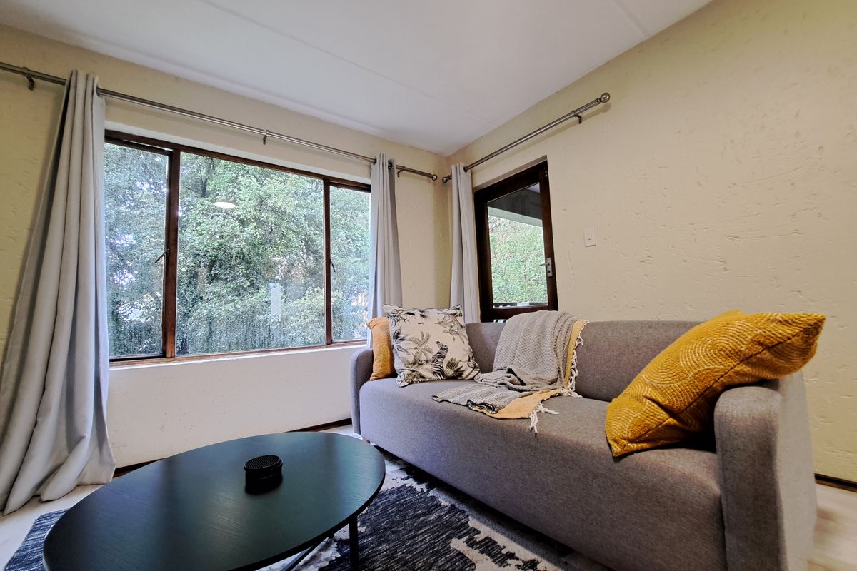 A cozy living room featuring textured walls and large windows that provide ample natural light and a view of the surrounding greenery.