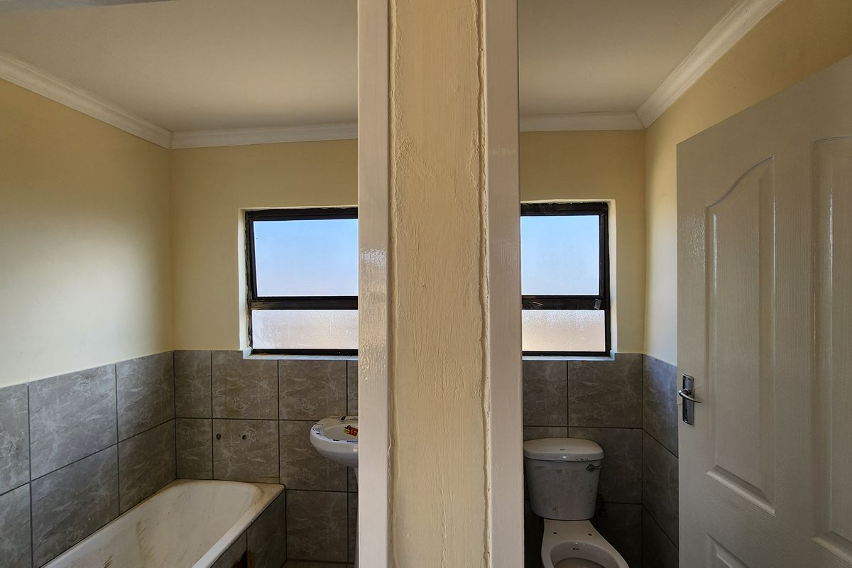 A functional bathroom featuring a bathtub, pedestal basin, and toilet, finished with partial wall tiling and neutral paint.