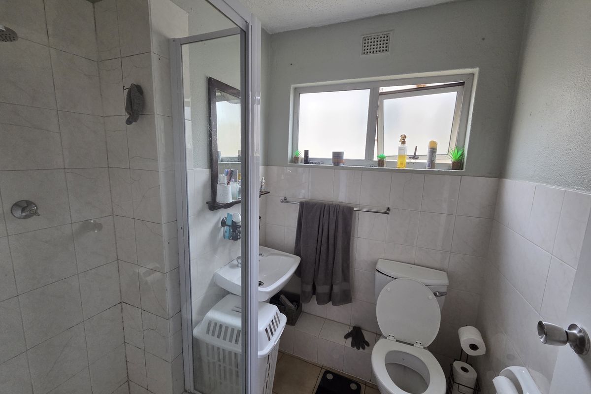 A functional bathroom featuring a shower enclosure, pedestal basin, and toilet with tiled finishes and natural light from a window.