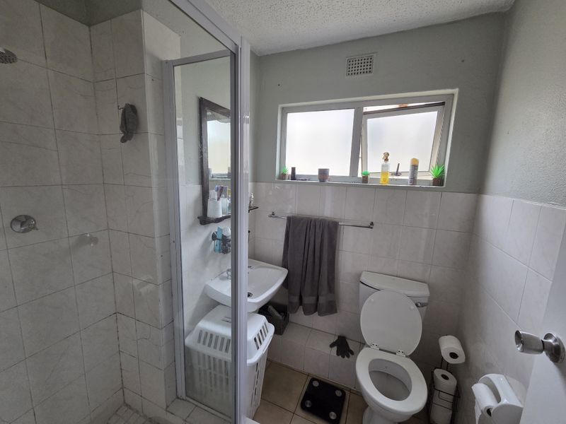 A functional bathroom featuring a shower enclosure, pedestal basin, and toilet with tiled finishes and natural light from a window.