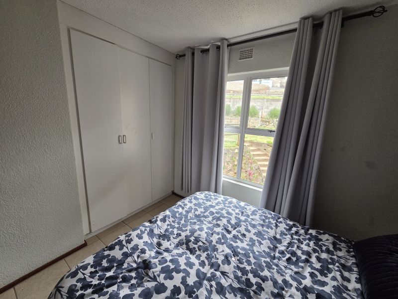 A functional bedroom featuring built-in cupboards, tiled flooring, and a window with views of the exterior garden area.