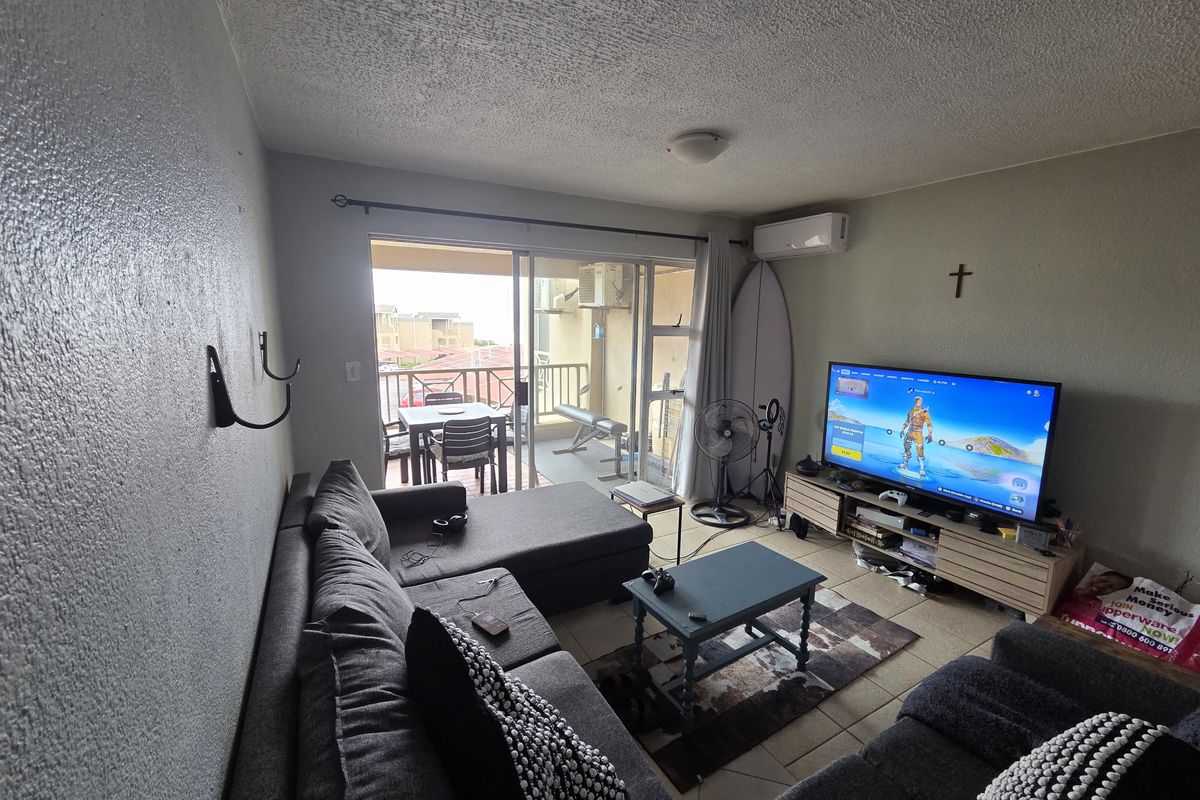 A living room featuring tiled flooring, a split-system air conditioner, and a sliding glass door providing access to a balcony.