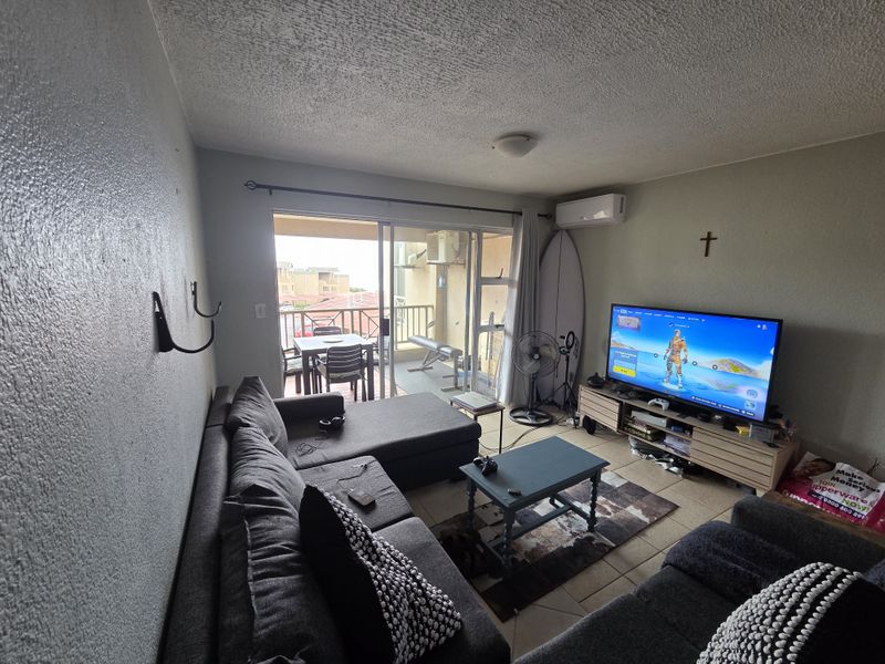 A living room featuring tiled flooring, a split-system air conditioner, and a sliding glass door providing access to a balcony.
