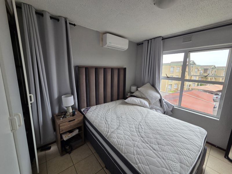 A bedroom featuring tiled flooring, an air conditioning unit, and a large window with views of the surrounding apartment complex.