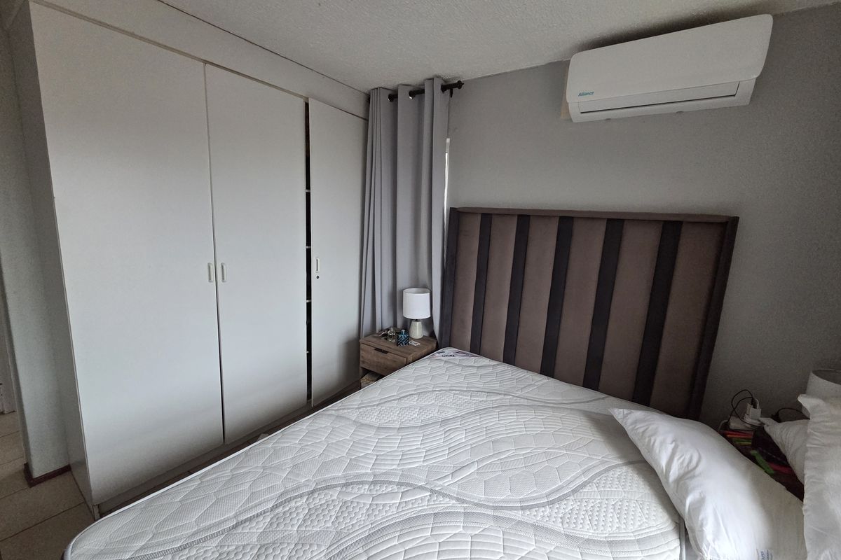 A functional bedroom featuring built-in cupboards, tiled flooring, and a wall-mounted split-system air conditioning unit for climate control.
