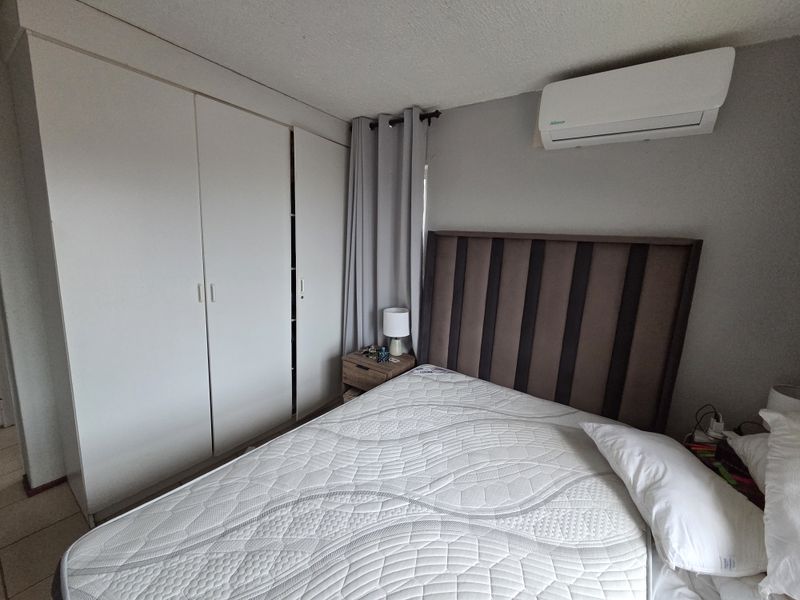 A functional bedroom featuring built-in cupboards, tiled flooring, and a wall-mounted split-system air conditioning unit for climate control.