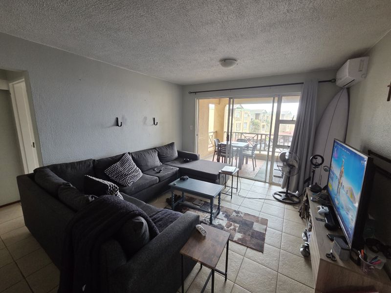 A living room featuring tiled flooring, a textured ceiling, and a sliding glass door leading to a balcony, equipped with a wall-mounted air conditioning unit.