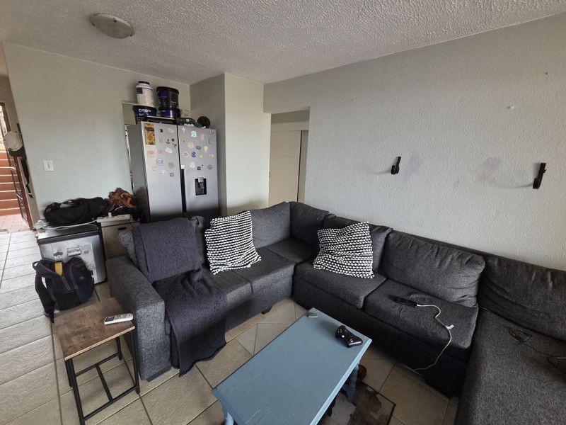 A living room area featuring tiled flooring and textured ceilings, currently showing signs of wear on the walls.