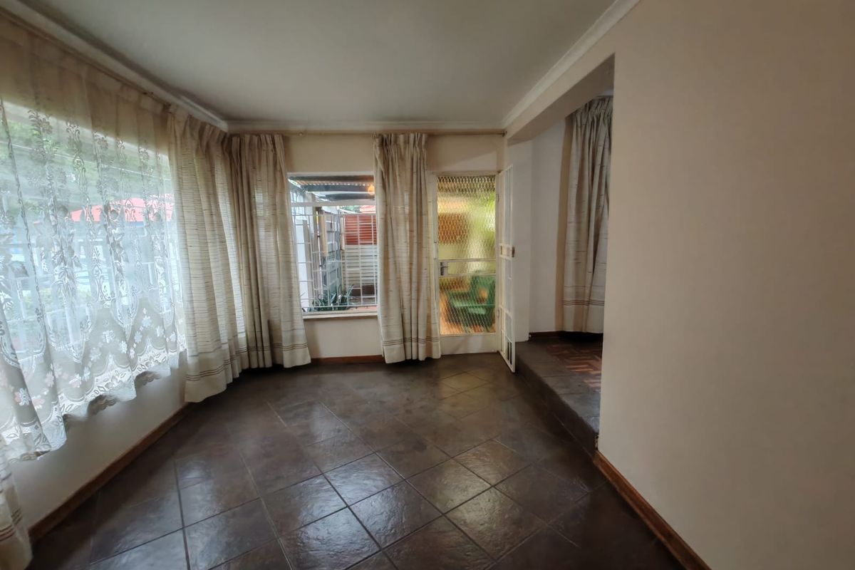 An empty living room featuring dark tiled flooring, large windows with curtains, and a security gate leading to an outdoor area.