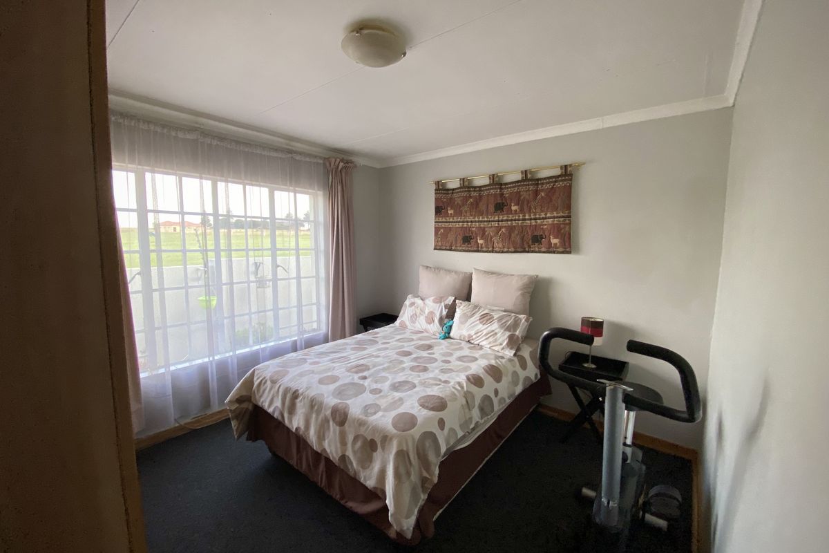 A functional bedroom featuring carpeted flooring, a large grid-pattern window allowing natural light, and standard ceiling lighting.