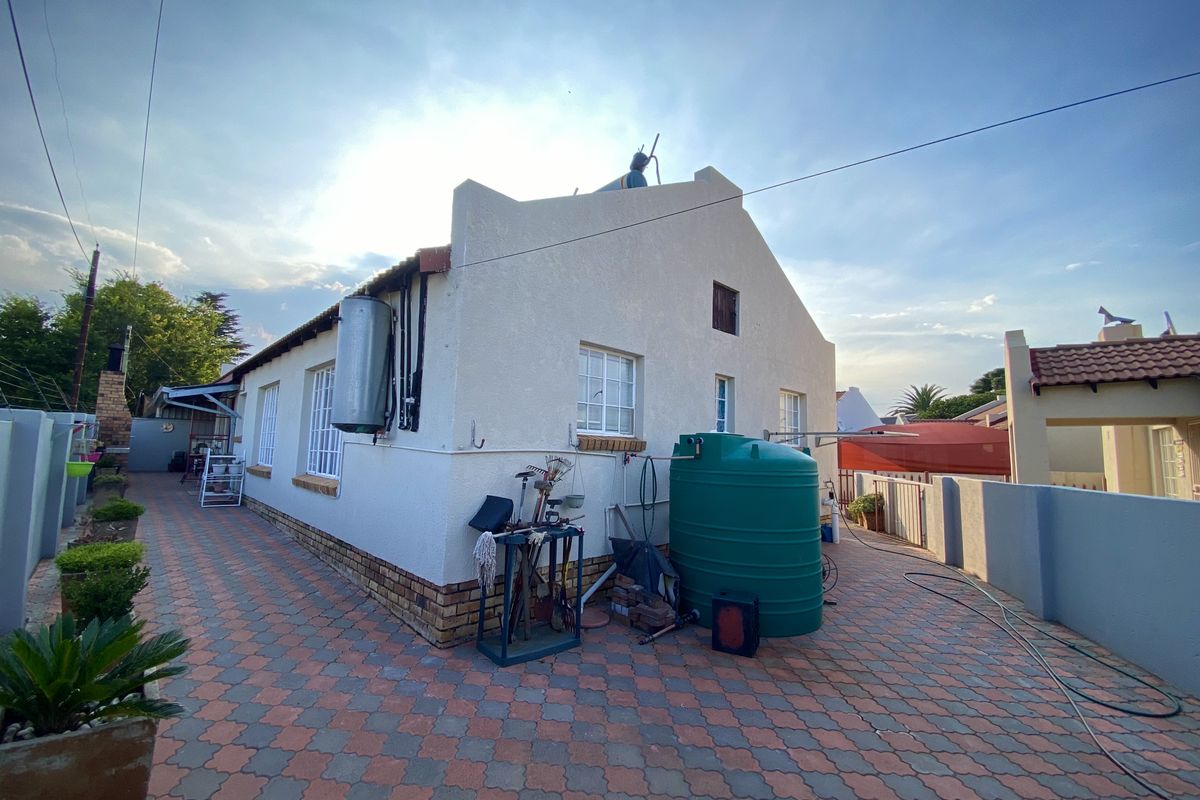 Rear exterior view of the property featuring a paved courtyard, external water storage tank, and wall-mounted geyser.