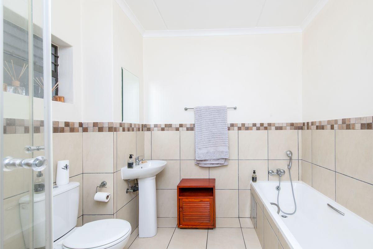 A functional bathroom featuring a pedestal basin, a standard bathtub with shower mixer, and neutral wall tiling with a decorative mosaic border.