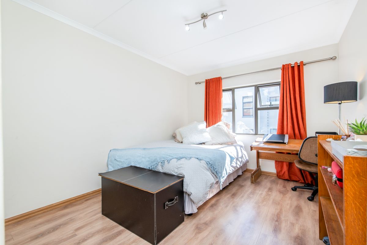 A well-lit bedroom featuring wood-look laminate flooring, a large window with curtain rod, and modern ceiling-mounted spotlight fixtures.