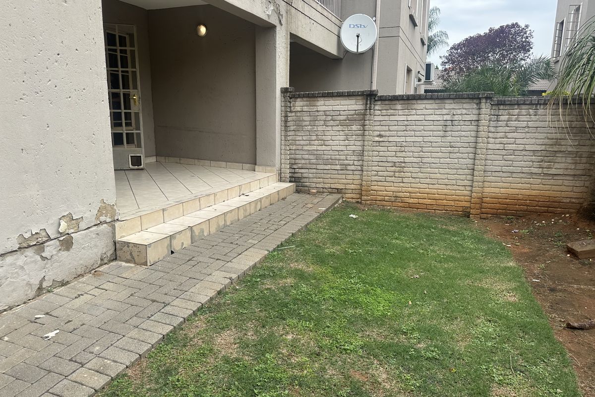 Rear view of the flat featuring a small tiled patio, paved walkway, private lawn area, and a brick boundary wall.