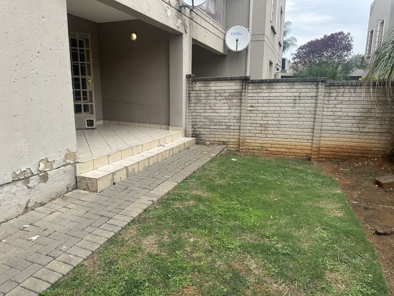 Rear view of the flat featuring a small tiled patio, paved walkway, private lawn area, and a brick boundary wall.