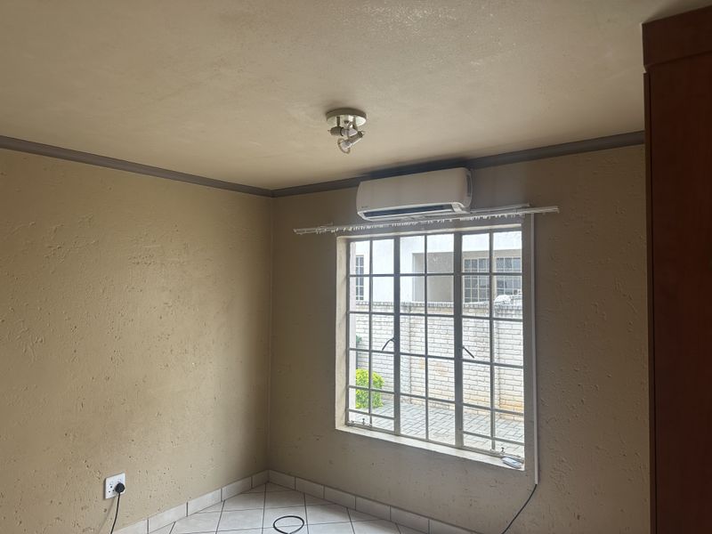An empty bedroom featuring tiled flooring, a wall-mounted air conditioning unit, and a window fitted with security bars.