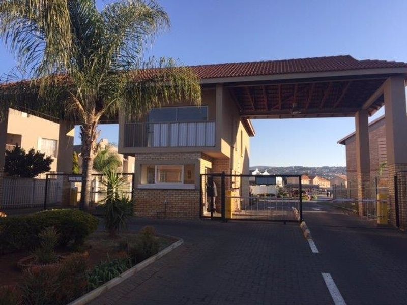 A secure residential complex entrance featuring a guard house, boom gate access, and paved driveway.