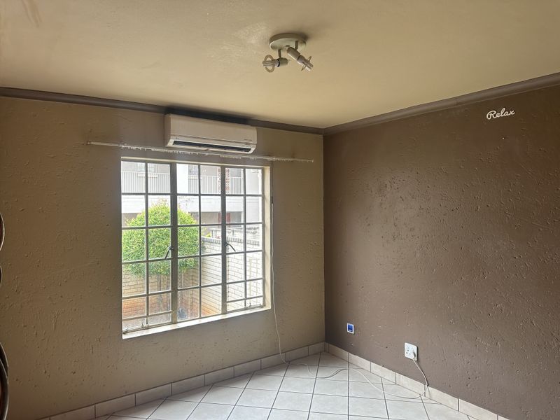 An empty bedroom featuring tiled flooring, a wall-mounted air conditioning unit, and a window with security bars.