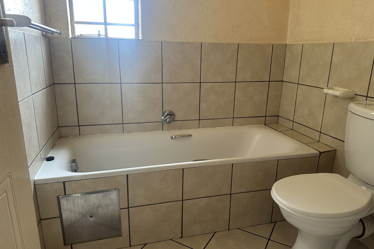 A functional bathroom featuring a built-in bathtub, toilet, and tiled finishes, requiring some cosmetic updates to improve its overall appearance.