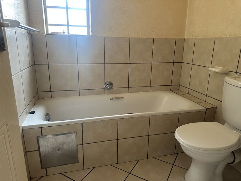 A functional bathroom featuring a built-in bathtub, toilet, and tiled finishes, requiring some cosmetic updates to improve its overall appearance.