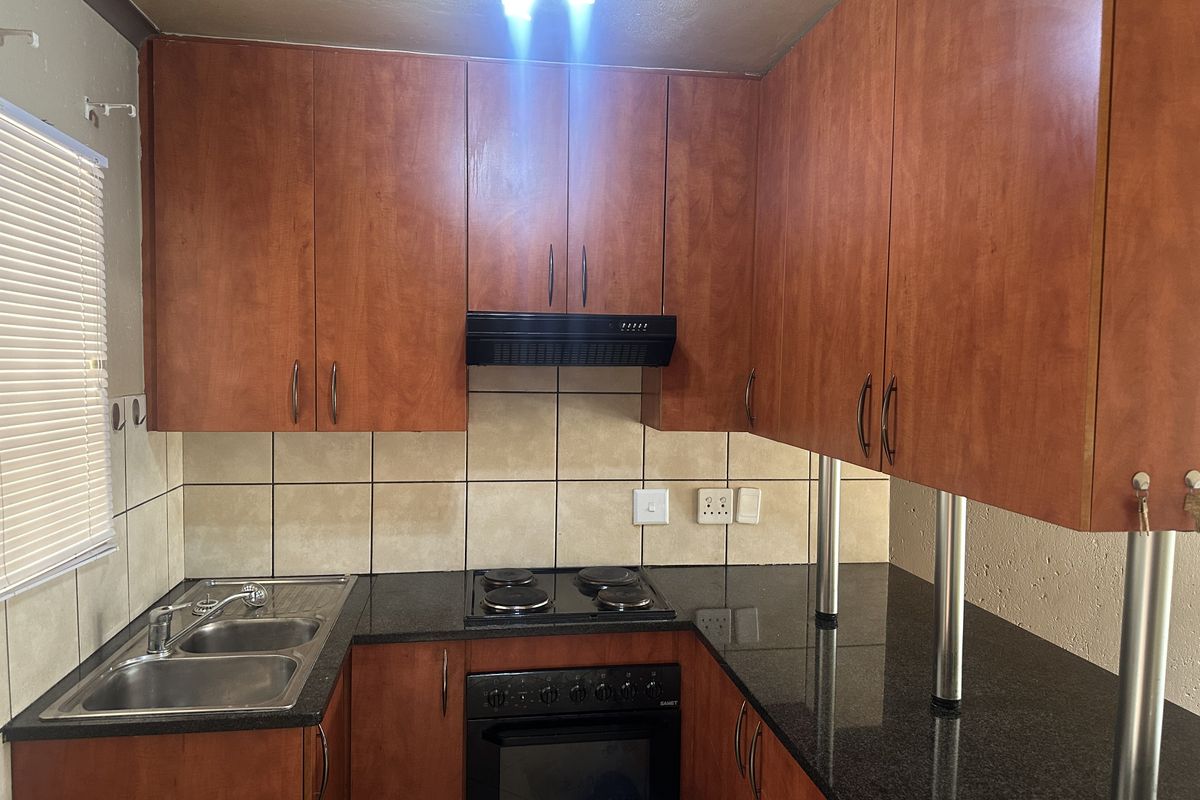 A functional kitchen featuring wood-finish cabinetry, granite countertops, a built-in oven with hob, and a tiled backsplash.