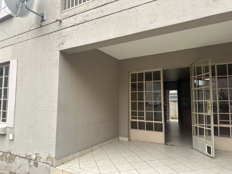 A covered patio area featuring tiled flooring and steel-framed glass doors leading into the interior, showing signs of exterior wall wear.