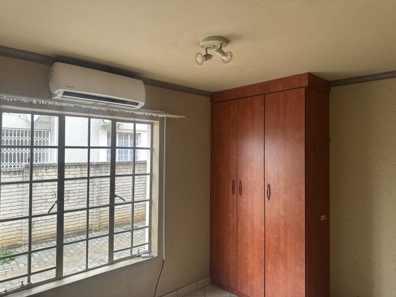 A bedroom featuring a built-in wardrobe, air conditioning unit, and security bars on the window, with tiled flooring throughout.