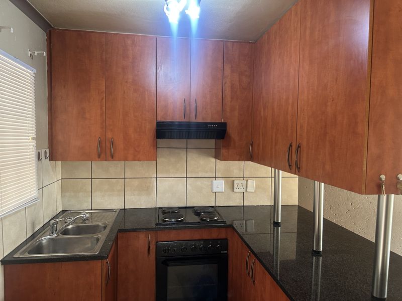 A functional kitchen featuring wood-finish cabinetry, granite countertops, a built-in oven with hob, and a tiled backsplash.