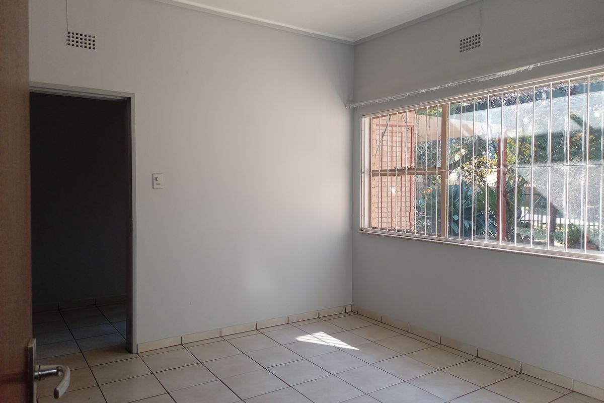 A bright, empty bedroom featuring neutral tiled flooring, large windows with security bars, and a clean, minimalist aesthetic ready for personalization.